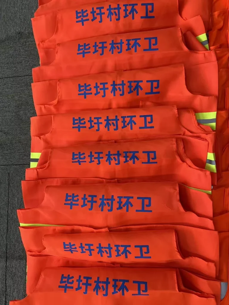 多件橙色反光背心背面印有蓝色村名和环卫文字